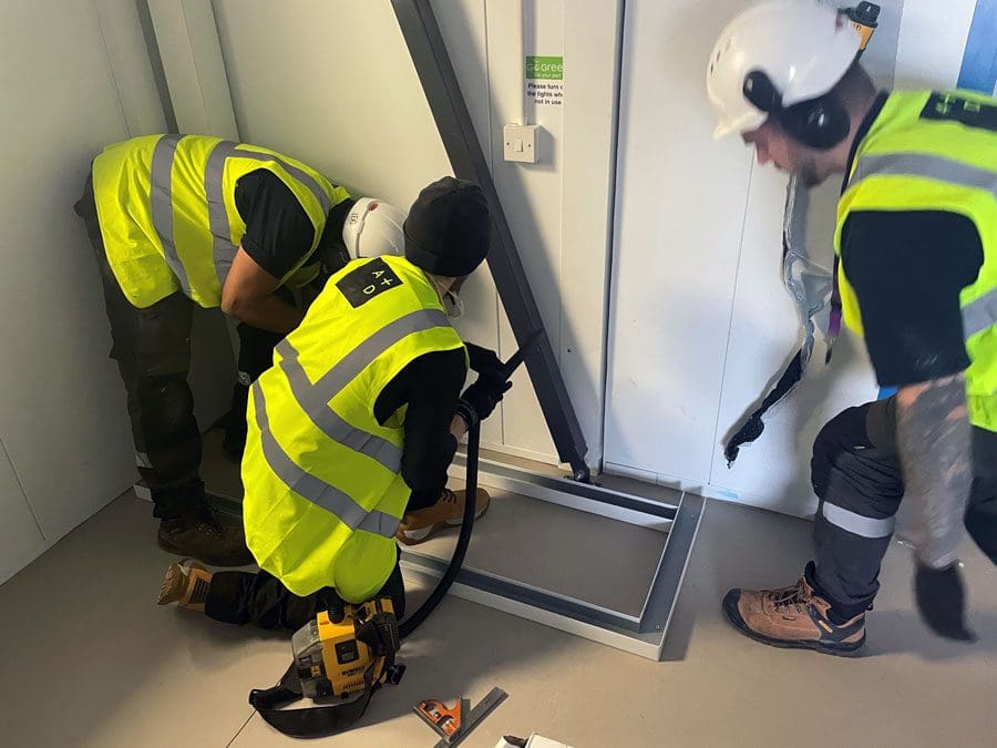 3 men in high visibility jackets installing some equipment to cleanroom